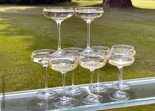 Classic coupe glasses of chilled champagne standing on top of other glasses on a table outdoors for a garden party