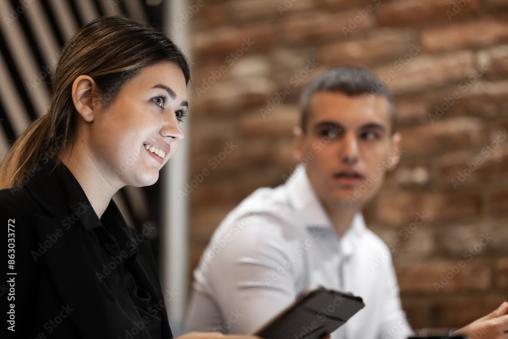 A young woman with a bright smile engages in a discussion with a male colleague in a contemporary brick office setting. A young woman with a bright smile engages in a discussion with a male colleague in a contemporary brick office setting.