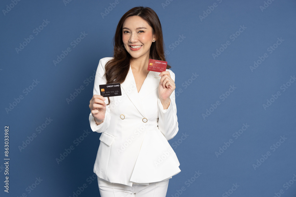 Young Asian businesswoman in white suit smiling, showing, presenting credit card for making payment or paying online business isolated on blue background