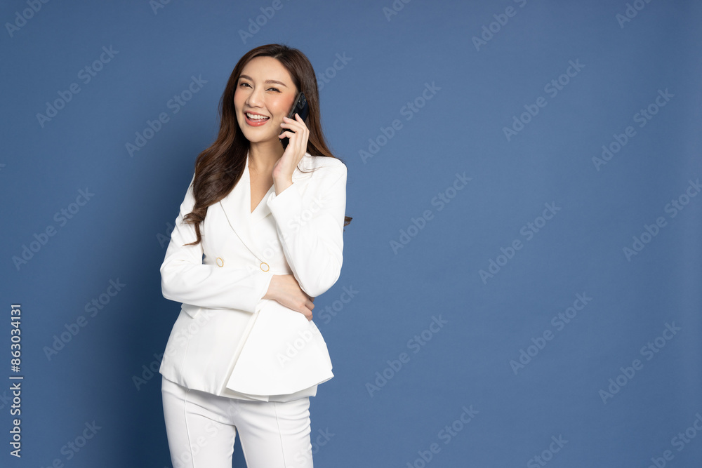 Young Asian businesswoman talking on mobilephone isolated on blue background Young Asian businesswoman talking on mobilephone isolated on blue background