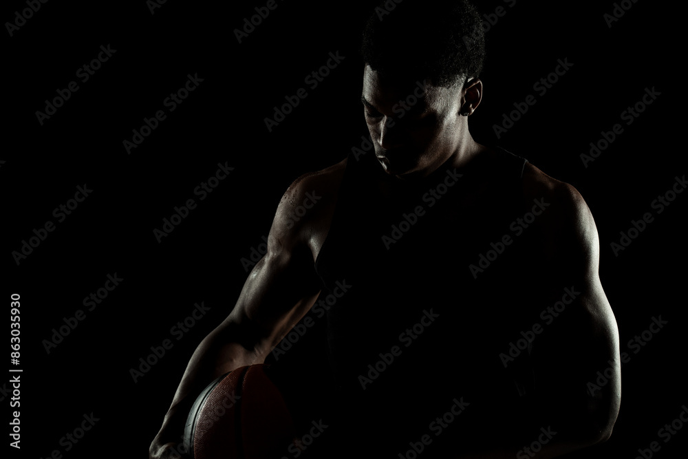 Basketball player holding a ball against black background. Serious concentrated african american man. Muscular person sidelit silhouette. Basketball player holding a ball against black background. Serious concentrated african american man. Muscular person sidelit silhouette.