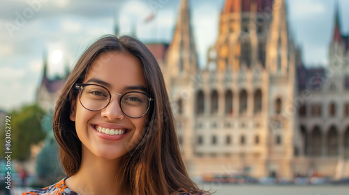 Uma jovem sorridente e de óculos fica em frente ao edifício do Parlamento de Budapeste, representando o charme urbano europeu. photo