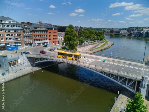 Yellow bus crossing a bridge over Sambre river in Namur, Belgium, on a sunny day. Aerial view.