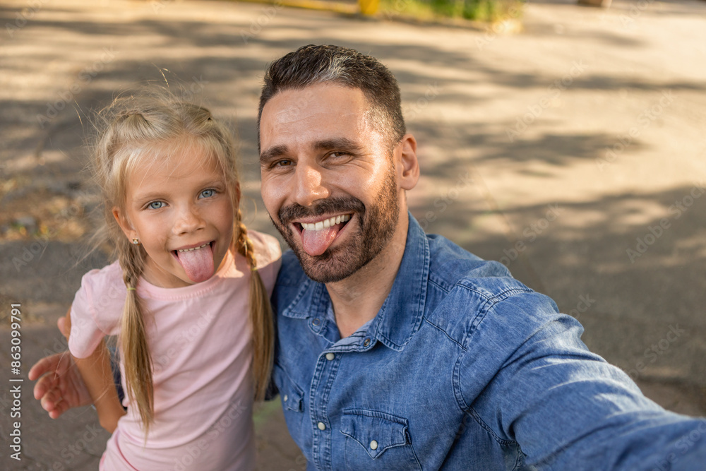 A father and his daughter are taking a selfie together outdoors. They are both smiling and sticking their tongues out playfully. They appear to be enjoying their time together. A father and his daughter are taking a selfie together outdoors. They are both smiling and sticking their tongues out playfully. They appear to be enjoying their time together.