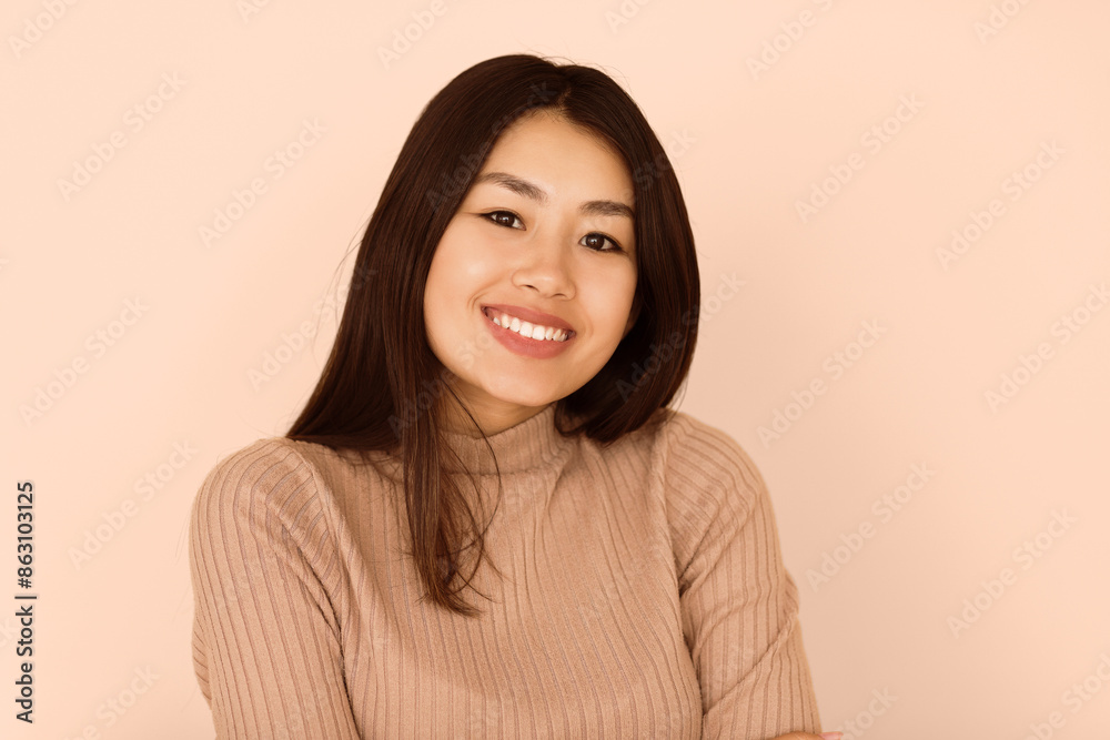 A young woman with long black hair smiles brightly against a beige backdrop. A young woman with long black hair smiles brightly against a beige backdrop.