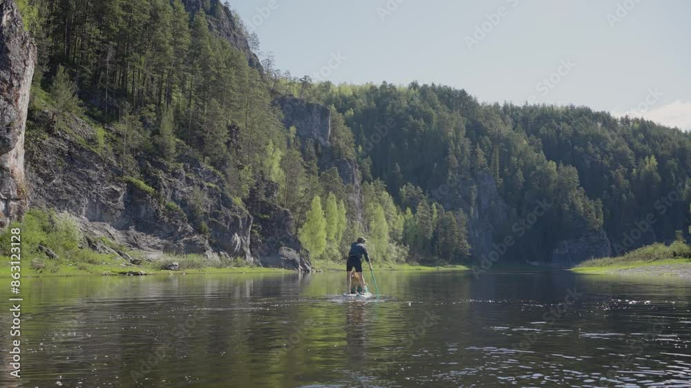 Man paddleboards with their dog on calm river, surrounded by lush forest and rocky cliffs, enjoying nature. Rafting on mountain river with his pet, guy is actively rowing with an oar. Man paddleboards with their dog on calm river, surrounded by lush forest and rocky cliffs, enjoying nature. Rafting on mountain river with his pet, guy is actively rowing with an oar.