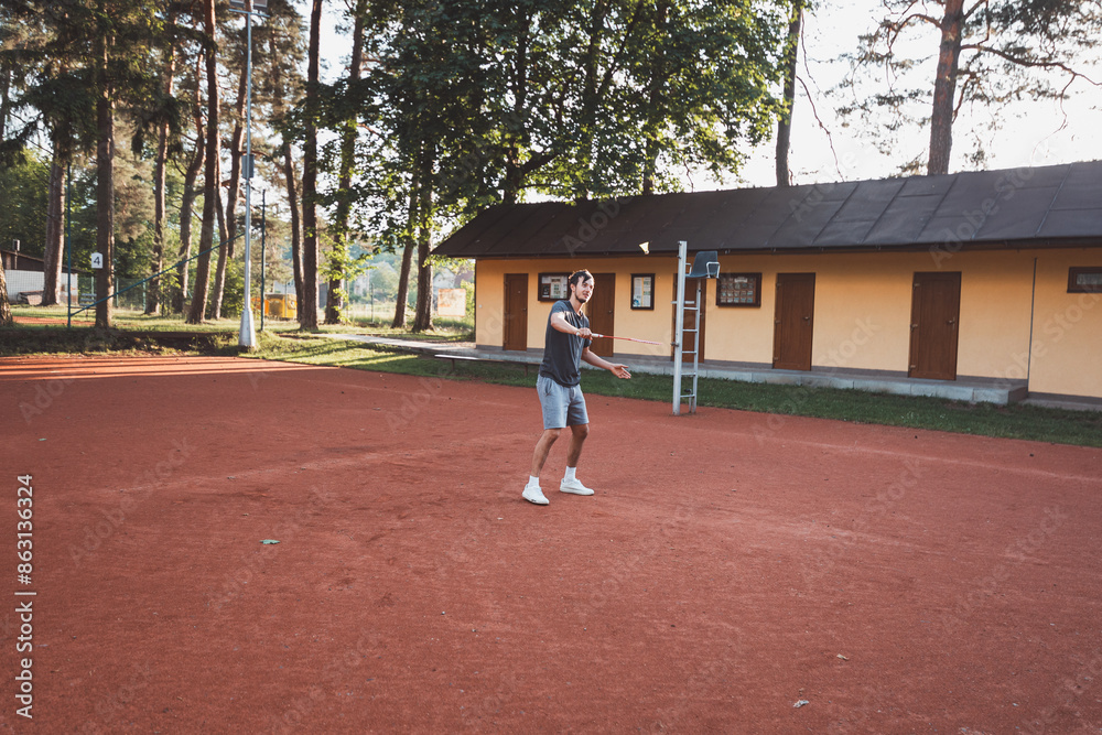 Black-haired athlete with a smile on his face plays badminton on a clay court. Enthusiasm for amateur sport. Learning new movement skills Black-haired athlete with a smile on his face plays badminton on a clay court. Enthusiasm for amateur sport. Learning new movement skills