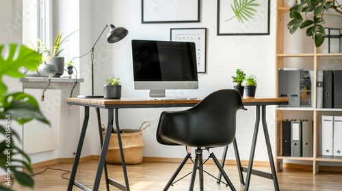 Black chair at table with computer monitor in bright home office interior with poster. Real photo