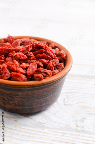 Dried goji berries in a brown ceramic bowl on a white wooden table. Superfood. Vegetarian, vegan. Healthy food concept. Vertical orientation.