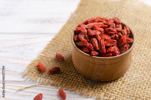Cuadro en lienzo Dried goji berries in a wooden bowl on a burlap cloth on a white wooden table