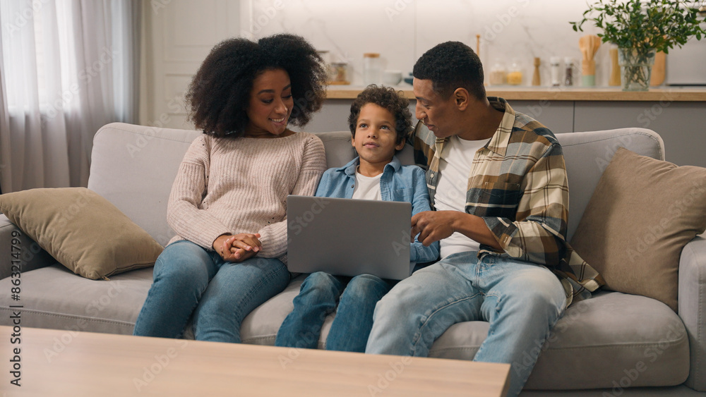 Happy married woman female mom male dad man African American family couple talking explain notebook pc software use internet app little boy child son kid living room couch. Parental control technology Happy married woman female mom male dad man African American family couple talking explain notebook pc software use internet app little boy child son kid living room couch. Parental control technology