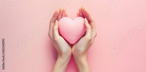 Female hands holding a pink heart on a pastel background, shown from above. A love concept for Valentine's Day cards or wallpaper with space