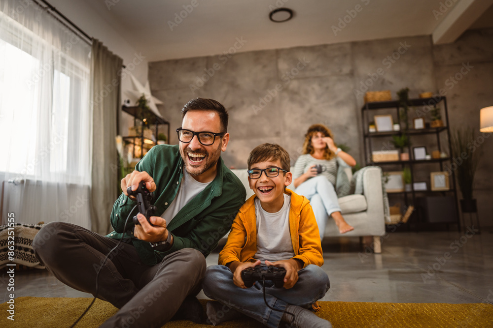 Dad and son play video games with joystick while mum wife watch them Dad and son play video games with joystick while mum wife watch them