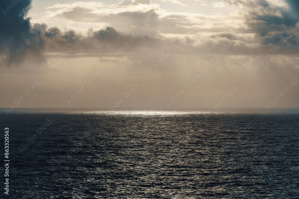 Fototapeta premium The sun is casting its rays through the clouds onto the ocean