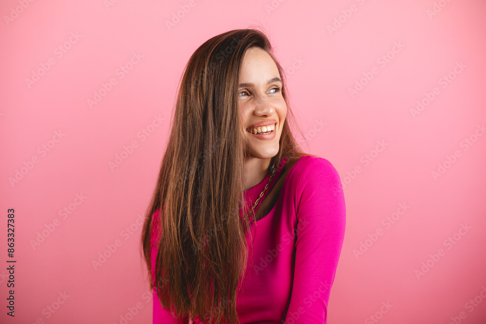 Happy cheerful young woman wearing pink long sleeves top rejoicing at positive news or birthday gift, looking at camera with joyful and charming smile. Brunette student girl isolated pink look at side