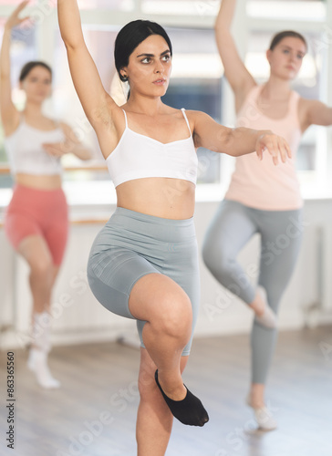 Enthusiastic young girl in casual sportswear practicing basic ballet movements with focus and grace during group dance class session in spacious studio