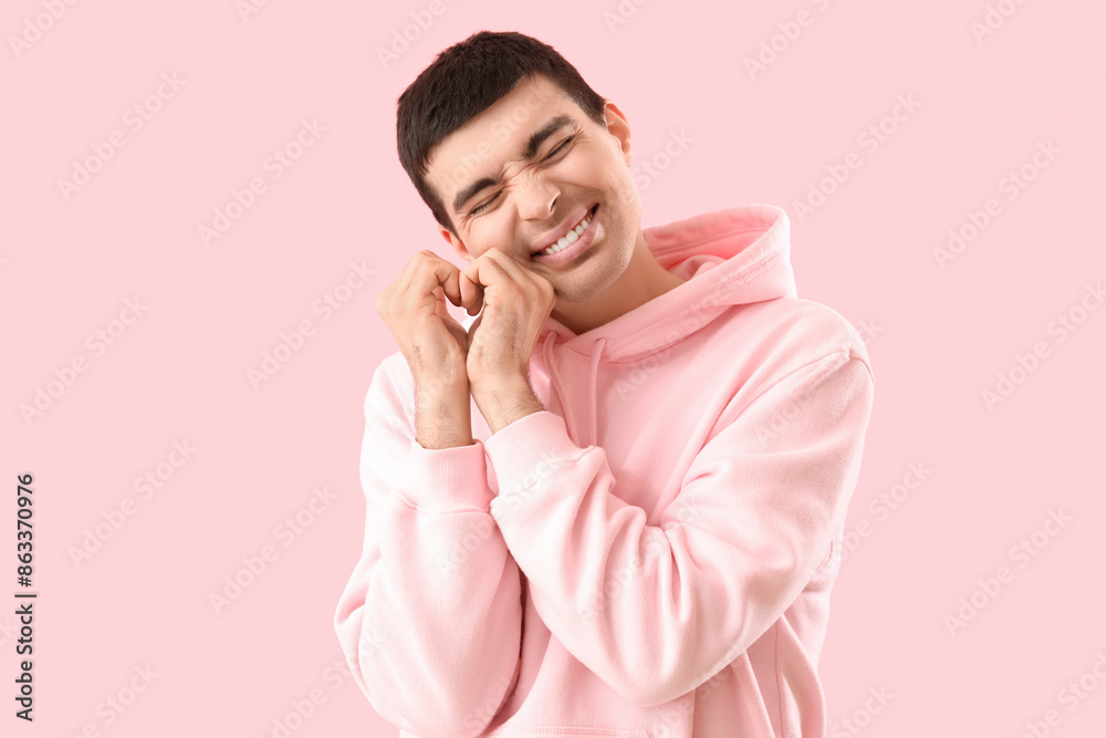 Young man making heart with his hands on pink background