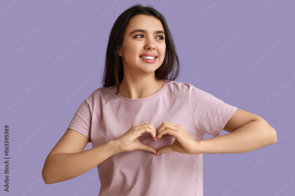 Beautiful young girl showing heart gesture on purple background. Valentine's Day celebration
