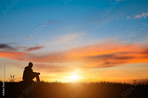 Silhouette of young man sits and praying alone at the top of the mountain at sunset with beautiful natural sunlight.