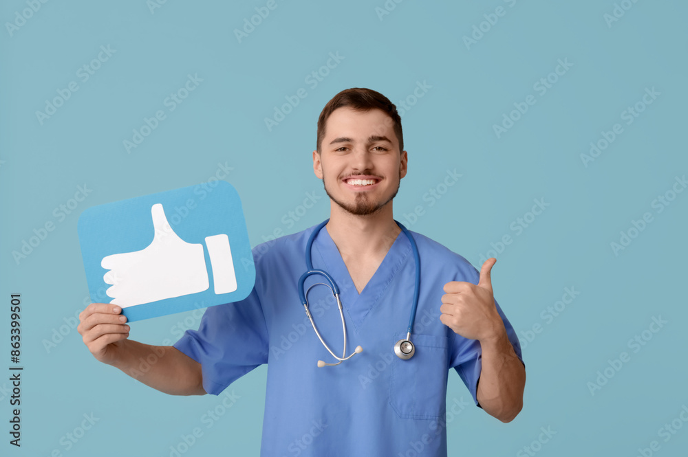 Handsome young happy male doctor with like icon showing thumb-up gesture on blue background Handsome young happy male doctor with like icon showing thumb-up gesture on blue background