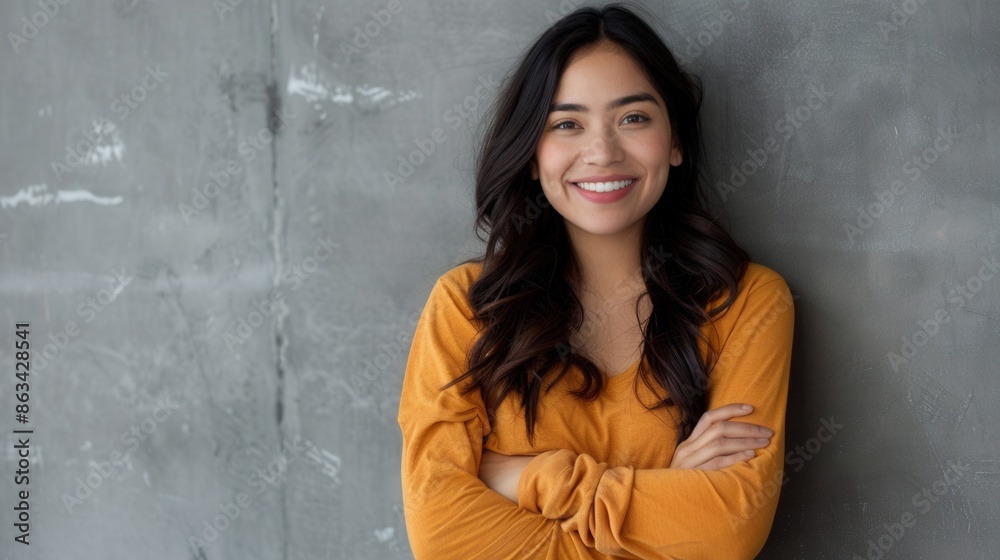 A young Hispanic woman smiles pleasantly while standing with crossed arms against a grey wall. She is looking directly at the camera. Generative AI A young Hispanic woman smiles pleasantly while standing with crossed arms against a grey wall. She is looking directly at the camera. Generative AI