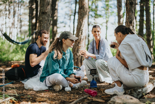 A group of friends enjoying a camping trip in the forest, sitting together and sharing a relaxing conversation amidst nature.