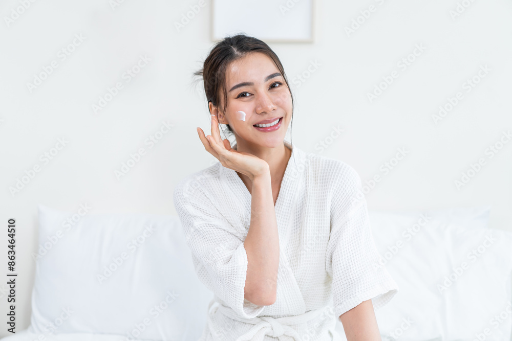 Portrait of Asian woman looking at camera while apply lotion on face. Portrait of Asian woman looking at camera while apply lotion on face.
