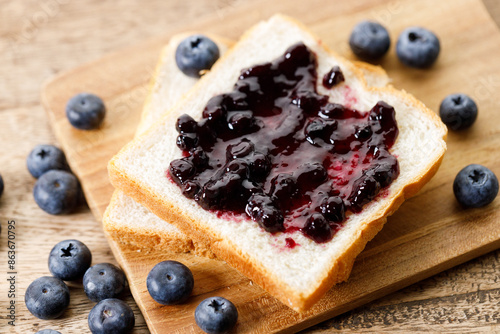 Blueberry jam with fresh berries on bread on rustic wooden table background. Selective focus.