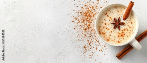Top view of a cozy cup of spiced chai latte with cinnamon sticks and star anise on a white background with scattered spices.