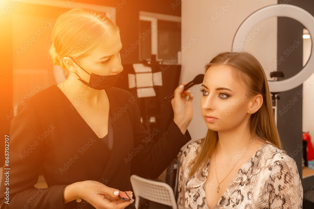Makeup beauty salon. Makeup artist applies powder and blush. Beautiful female face. Makeup master's hand puts blush on cheeks of beauty model girl. Makeup in progress Makeup beauty salon. Makeup artist applies powder and blush. Beautiful female face. Makeup master's hand puts blush on cheeks of beauty model girl. Makeup in progress