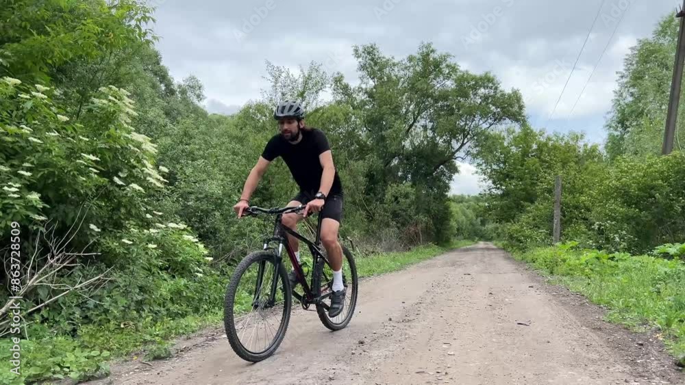 Man cycling on tranquil rural dirt road surrounded by lush greenery and trees under a cloudy sky Man cycling on tranquil rural dirt road surrounded by lush greenery and trees under a cloudy sky