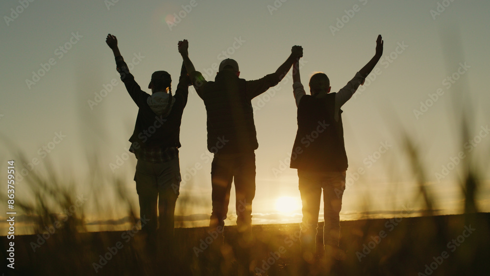 In the evening glow, a family of farmers stands in their field, raising their hands in a triumphant gesture of success.