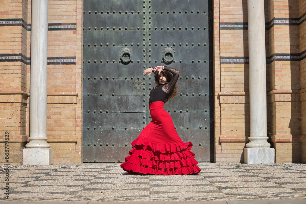 Young, beautiful, brunette woman in black shirt and red skirt, dancing flamenco in front of an old, black metal door. Flamenco concept, dance, art, typical Spanish. Young, beautiful, brunette woman in black shirt and red skirt, dancing flamenco in front of an old, black metal door. Flamenco concept, dance, art, typical Spanish.