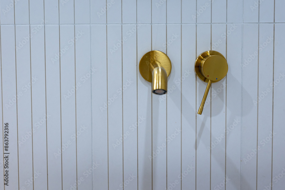 Bronze bathroom water tap in a bathroom finished with white tiles. Minimalist bathroom finish. Photographed in natural light.