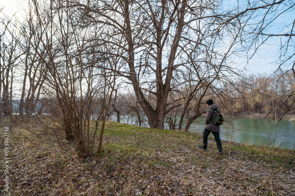 A teenage boy walking along the riverbank and forest, early spring landscape, the concept of hiking and outdoor activities A teenage boy walking along the riverbank and forest, early spring landscape, the concept of hiking and outdoor activities