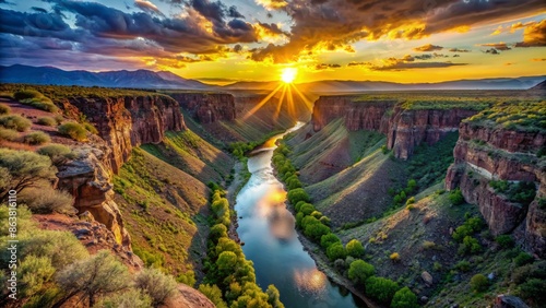Serene sunrise over the Rio Grande River flowing through the Taos Gorge, with rugged cliffs and lush green vegetation surrounding.
