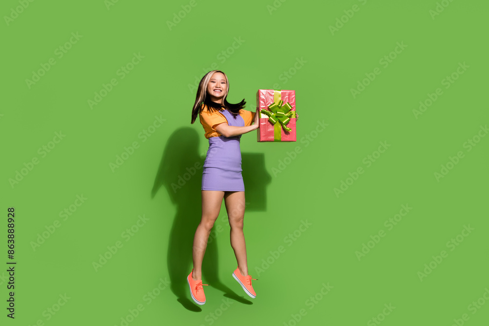Full length photo of lovely young lady hold gift jumping dressed stylish violet yellow garment isolated on green color background