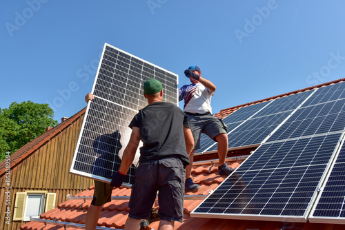 Dachdecker beim Aufbau einer Photovoltaikanlage auf einem neu gedeckten Ziegeldach: Das Schienensystem ist montiert und die Paneele werden auf das Schienensystem aufgesetzt