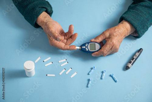 Elderly female hands with a blood glucose meter and lancets. photo