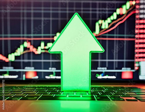 Illuminated green arrow pointing upwards in front of trading chart on computer 