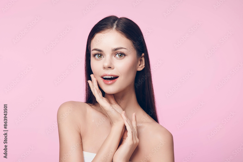 Beautiful young woman with clear skin on a pink background, looking at the camera with her hands on her face Beautiful young woman with clear skin on a pink background, looking at the camera with her hands on her face