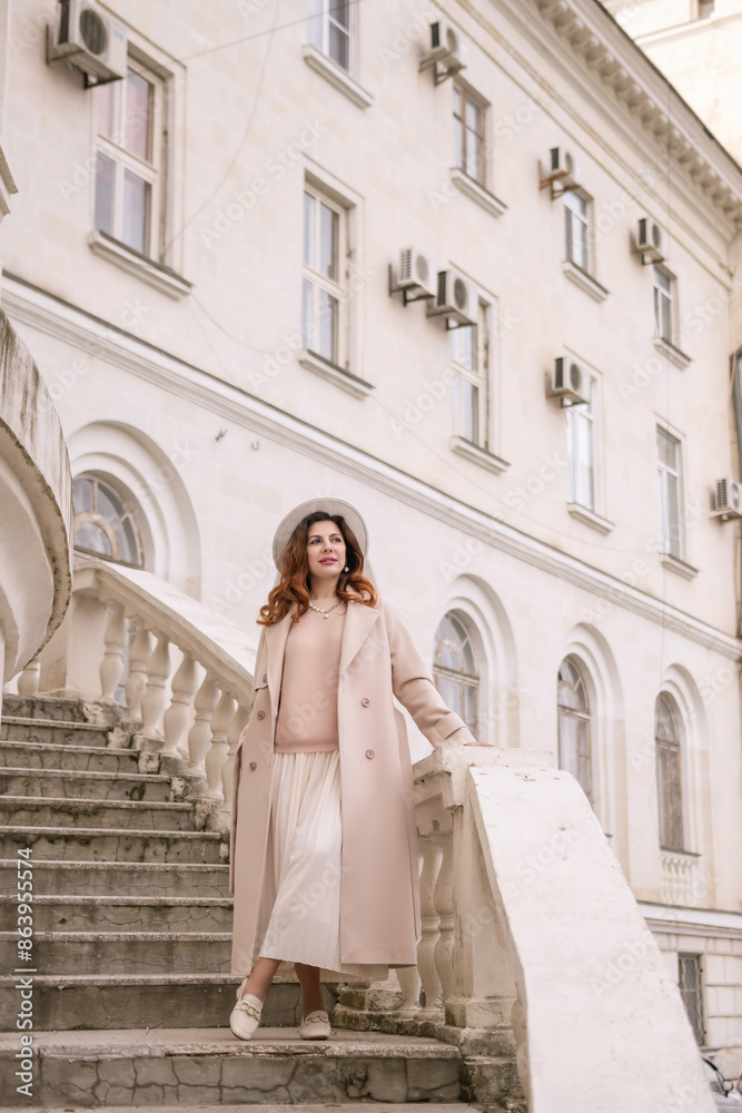 Obraz premium woman in elegant coat and hat against an intricate architectural backdrop, harmoniously blending modern fashion with historical allure. The soft daylight adds to its timeless appeal.