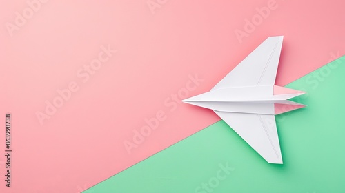 Flat lay of white paper plane on pastel pink and green background with text space 