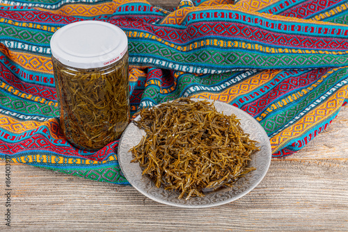 Fresh leaves of the zahter (Thymbra spicata) used to add the green salads with olive oils. Black thyme (zahter) with olive oil in a glass jar. Zahter on wooden background. Mediterranean food. photo