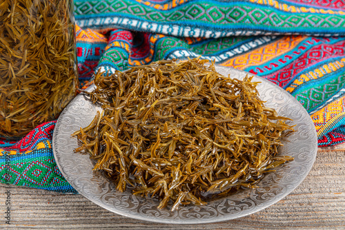 Fresh leaves of the zahter (Thymbra spicata) used to add the green salads with olive oils. Black thyme (zahter) with olive oil in a glass jar. Zahter on wooden background. Mediterranean food. photo