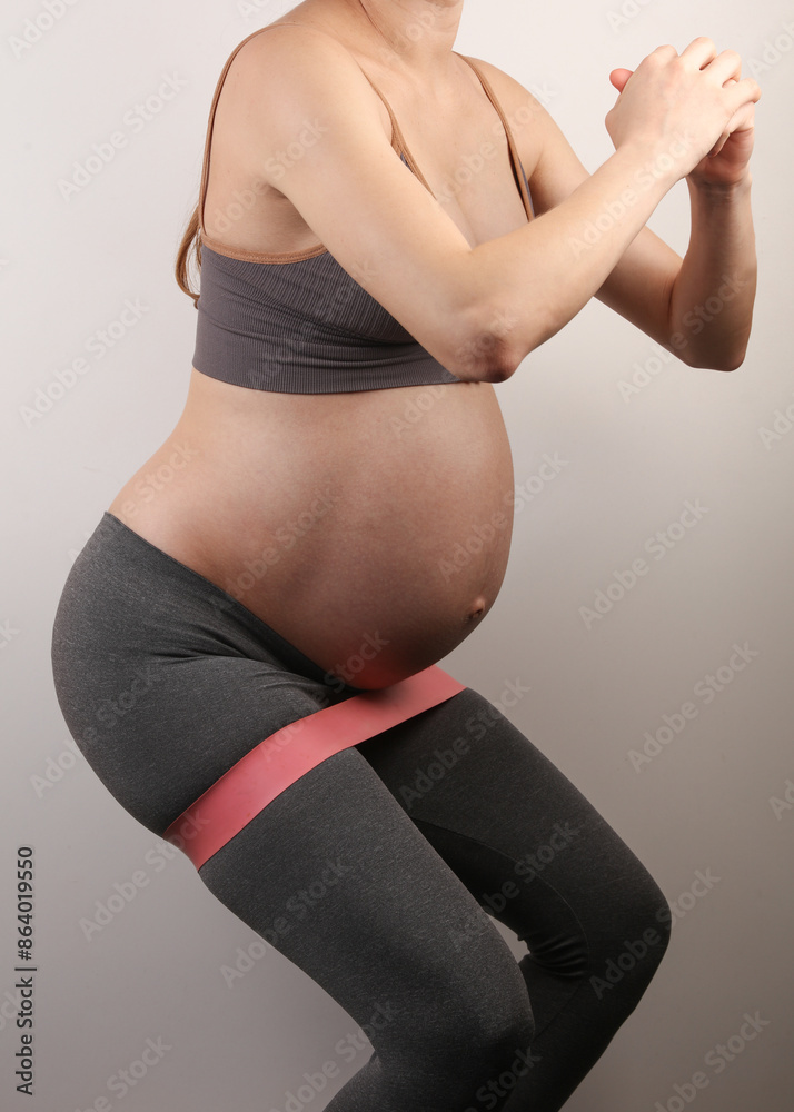 Fototapeta premium Pregnant woman exercising with fitness bands on gray background