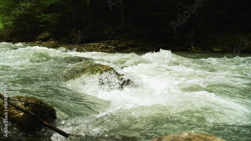 Close-up of a fast-flowing river cascading over boulders at the bottom. Low angle. Exuberance and natural power of the river. Slow motion photo