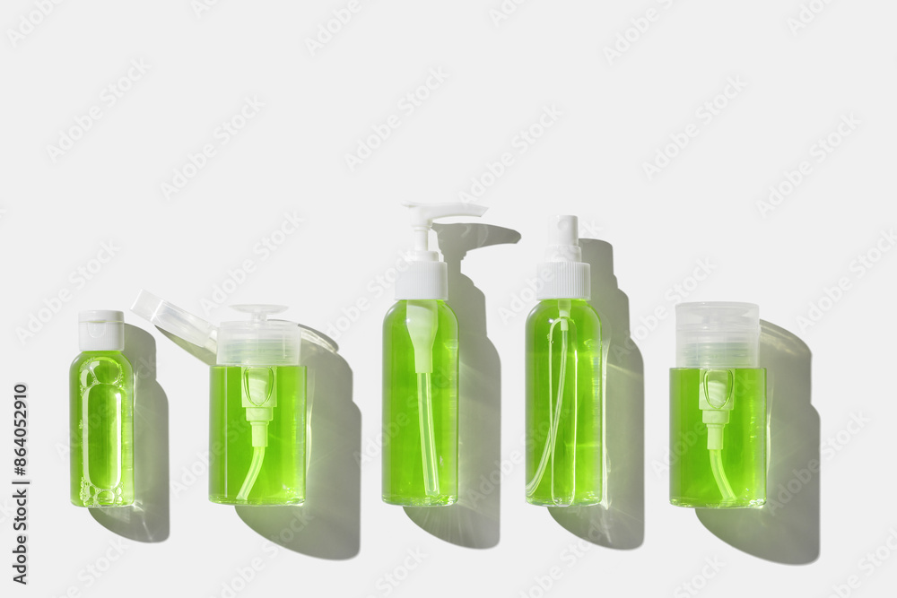 Cosmetic products with green lime liquid for skin treatment, beauty routine, skin health. Minimal top view with lotion, tonic, gel, micellar water mockup with sun shadow, isolated on white