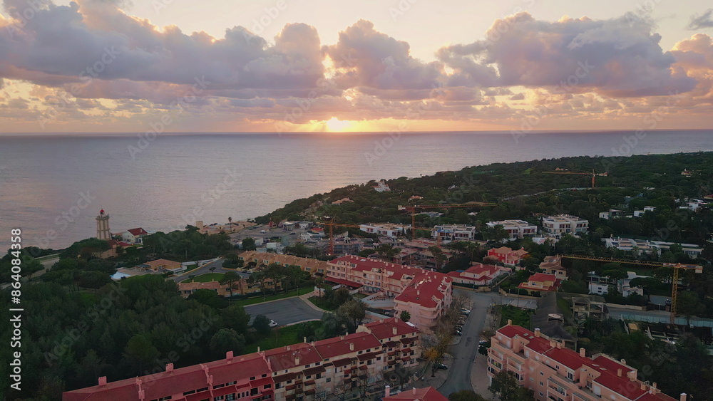 Fototapeta premium Coastal city bathed sunset glow near lighthouse. Aerial view tranquil seascape 