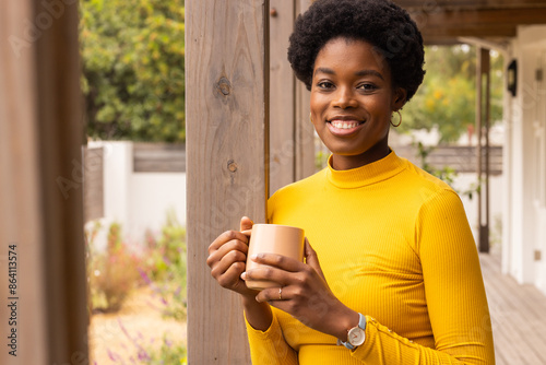 Smiling woman in yellow sweater holding coffee cup on porch, enjoying morning